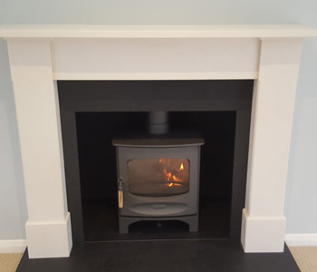 Charnwood C5 Woodburner - in gun metal with a honed granite hearth and limestone fire surround Alice in New Crème. Installed in West Clandon near Guildford, Surrey
